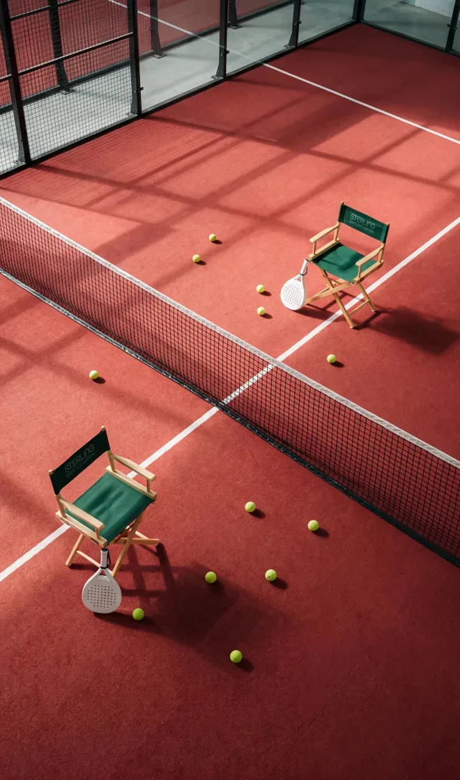 A red padel court with director's chairs and tennis balls